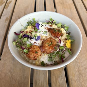 3128 Social House - Seared scallops on Lobster Risotto 12 out of 10 - A white bowl holds a dish with fried pieces, microgreens, and edible flowers, placed on a wooden table with slats. The dish appears to be a gourmet presentation with fresh garnishes and a foam or sauce element. - Gastropubs Near Me - Albuquerque, New Mexico