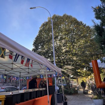 Wadadli - Love how the sun was shining through the smoke and tree - Street scene featuring a vendor stall with international flags, large trees, and sunlight filtering through the leaves. - Caribbean Near Me - Brooklyn, New York