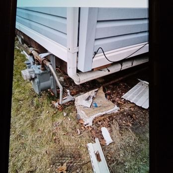JF Keevill Construction - Trash left to blow everywhere - Debris, including torn cardboard, plastic, and a piece of siding, is scattered on the ground near the house's foundation and siding. - Electricians Near Me - West Chester, Pennsylvania