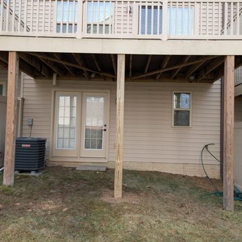 Mr Everything Md Construction - After - A backyard area with a deck above, a door, a window, and outdoor utility equipment, including an air conditioning unit and a garden hose. - General Contractors Near Me - Glen Burnie, Maryland