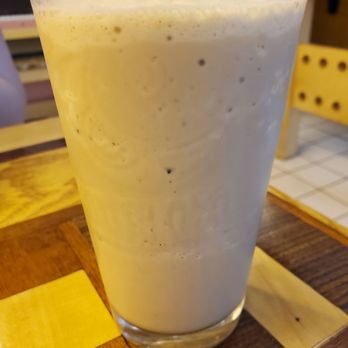 Caffe Casa - Frozen chai - A tall glass filled with a creamy, frosty chai beverage with visible specks of spices, placed on a wooden table in a cafe setting. - Bakeries Near Me - Kalamazoo, Michigan