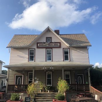 Mars Brew House - Best coffee in town - A two-story building with a sign for Mars Brew House, featuring a porch with potted plants and outdoor seating, under a partly cloudy sky. - Coffee & Tea Near Me - Mars, Pennsylvania