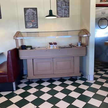 Gabby's Diner - Salad bar - A salad bar with a glass sneeze guard, placed against a wall with chalkboard menus, in a diner with checkered floor tiles. - American Near Me - Milan, New Mexico