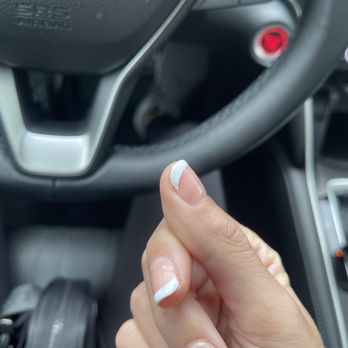 Legend Nails - Frankfort - Nails - A hand with a French manicure is positioned inside a car, close to the steering wheel and dashboard controls. - Nail Salons Near Me - Frankfort, Illinois