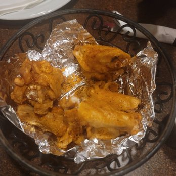 Fire Slice Pizzeria - BBQ Bone in Wings - Fried chicken wings are placed in a black wire basket lined with aluminum foil, on a dark brown table. The wings are seasoned and cooked. - Pizza Near Me - Amarillo, Texas