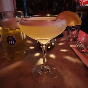 Werkstatt - Lemon drop martini - A lemon drop martini in a coupe glass with a lemon wedge garnish on the rim, placed on a restaurant table. The table has a warm, dim lighting ambiance with star-shaped candle holder reflections. In the background, there are glasses, a fork, and a napkin, indicating a dining setting. - Austrian Near Me - Brooklyn, New York