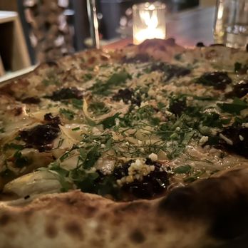 Prairie Fire - Potato pizza with spicy sausage - A pizza with a crispy crust topped with herbs, greens, and dark sauce, served in a dimly lit restaurant setting. - Pizza Near Me - Brookline, Massachusetts
