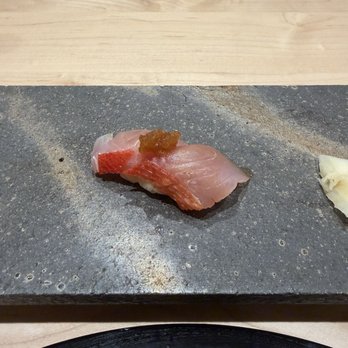 Two Nine - A slice of sashimi with a small amount of sauce or condiment on top is presented on a dark stone plate, with a wooden surface in the background. - Sushi Bars Near Me - Washington, DC, District of Columbia
