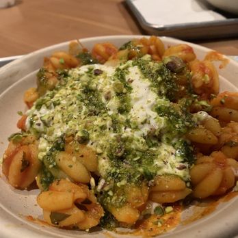 Tulipani - Pomodoro pasta with buratta and pistachios - A bowl of pasta with a tomato-based sauce, topped with green pesto, crumbled cheese, and chopped pistachios, served at a restaurant. - Pasta Shops Near Me - Albuquerque, New Mexico