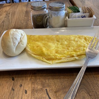 Rustiko - Cheese omelete - A rectangular white plate holds a cheese omelette, a bread roll, and a fork, with salt and pepper shakers and sugar packets in the background. - Kosher Near Me - Surfside, Florida