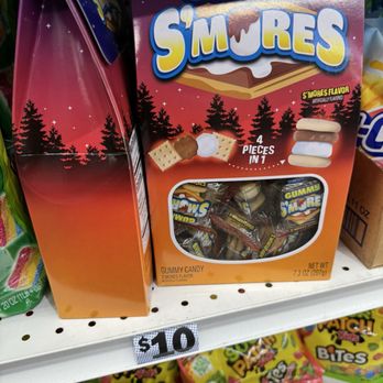 Five Below - Not everything is $5 or below. - The image shows a box of Gummy S'mores candy on a store shelf, with a prominent price tag of $10 below it. The box has bright, colorful packaging with images of the candy and a window revealing individually wrapped pieces inside. The packaging indicates the flavor as S'mores and contains four pieces in one package. Surrounding items include other snack products on the shelf. - Discount Store Near Me - Oxnard, California