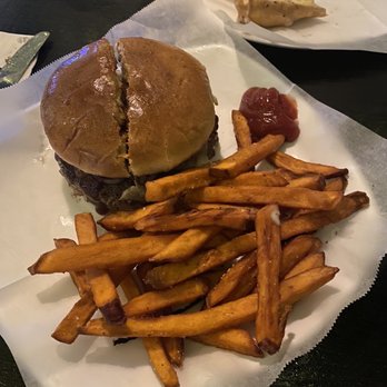 The Corner Pub - BYO burger - A burger with a bun, French fries, and a small serving of ketchup on a white tray at a restaurant. In the background, a plate with a slice of pie and a cup of sauce is visible. - Dive Bars Near Me - Boston, Massachusetts