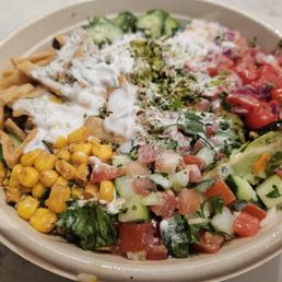 A colorful salad in a bowl containing corn, chopped cucumbers, tomatoes, and various vegetables with dressing.
