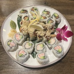 Spicy California Roll - A white plate holds various sushi rolls, including California rolls and other specialty rolls, garnished with wasabi, pickled ginger, lemon, and an orchid flower.