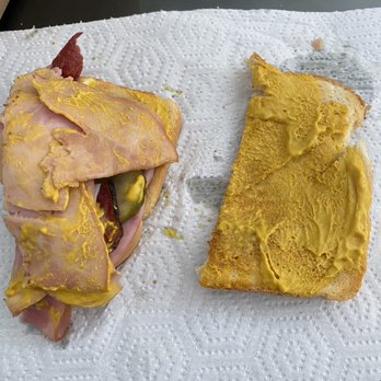 Inxpot - This one side of half the sandwich. This overflow of mustard occurs on both sides. - A sandwich with ham, salami, and mustard is placed on a paper towel, alongside a piece of bread with mustard spread on top. - Coffee & Tea Near Me - Keystone, Colorado