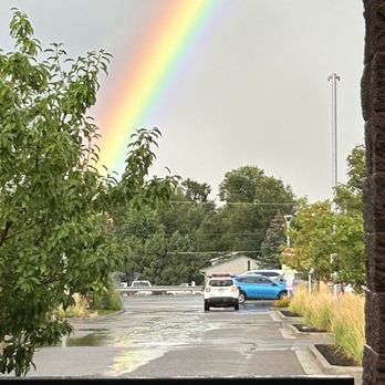 Illegal Pete's - Table Mesa - Illegal Pete Table Mesa - A rainbow is visible in the sky over a parking lot, with trees and parked cars, seen from a window with a railing. - Bars Near Me - Boulder, Colorado