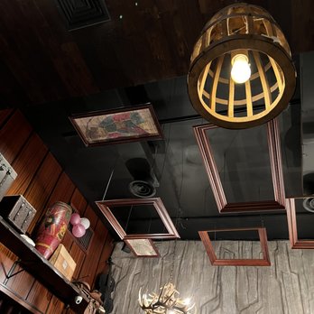 Tavern 157 - Ceiling Decor Pt.2 - The ceiling features wooden picture frames, a chandelier resembling antlers, and a wooden pendant light with an exposed bulb, in a room with dark wood paneling and textured wall. - Lounges Near Me - Flushing, New York