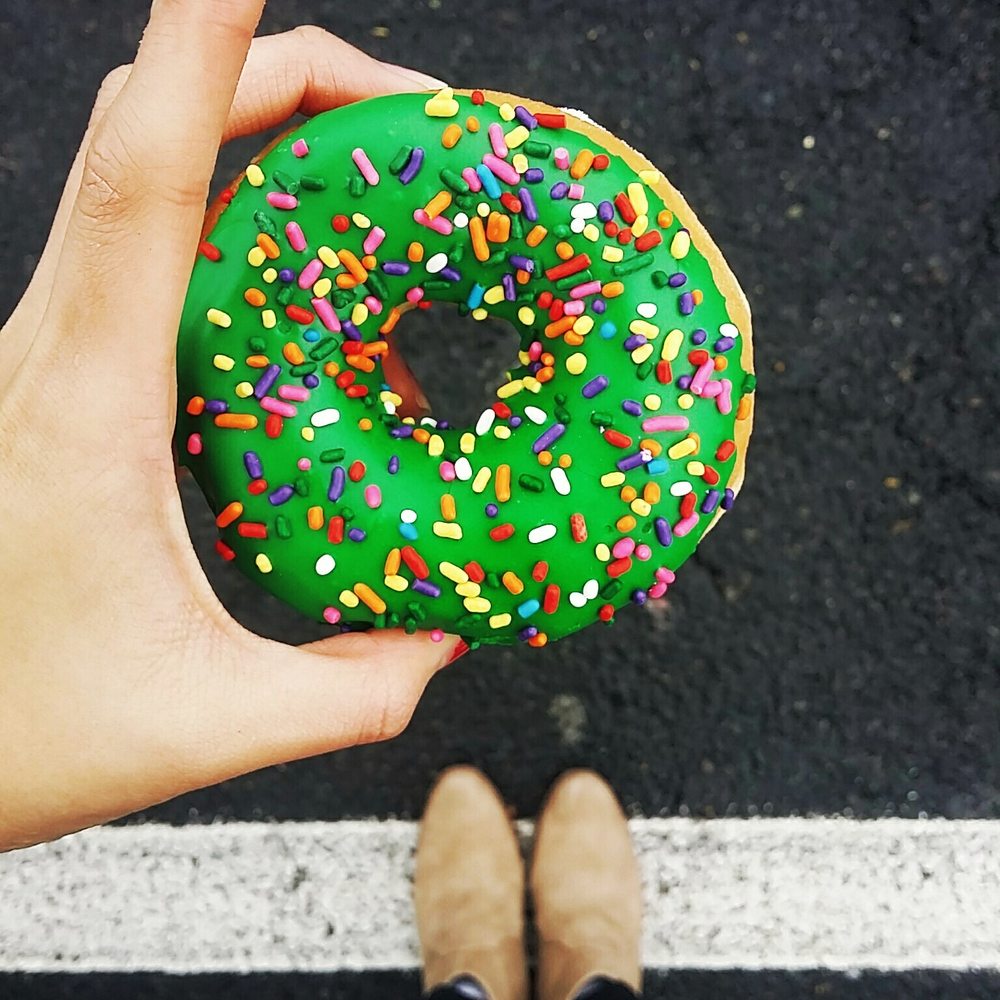 a person holding a green donut with sprinkles a person holding a green donut with sprinkles