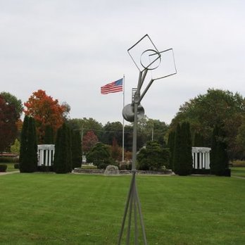 Mount Saint Mary Park - A metallic abstract sculpture is situated in a park with green grass, trees, and an American flag flying in the background. - Botanical Gardens Near Me - St. Charles, Illinois