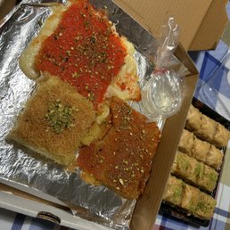 Kunafa and baklava (small) - A tray of Middle Eastern desserts featuring knafeh with pistachios and baklava, accompanied by a small glass of water, on a table with a checkered tablecloth.