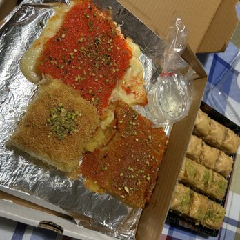 Kunafa King - Kunafa and baklava (small) - A tray of Middle Eastern desserts featuring knafeh with pistachios and baklava, accompanied by a small glass of water, on a table with a checkered tablecloth. - Middle Eastern Near Me - Ajax, Ontario