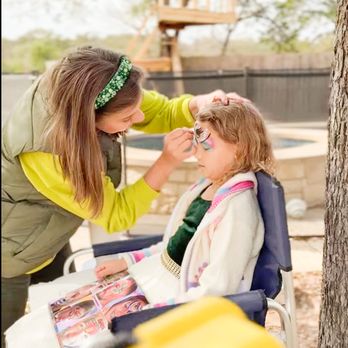 The Playwell Club - A child getting face paint outdoors, sitting calmly while an artist adds colorful details in a relaxed backyard party setting. - Venues & Event Spaces Near Me - Round Rock, Texas The Playwell Club - A child getting face paint outdoors, sitting calmly while an artist adds colorful details in a relaxed backyard party setting. - Venues & Event Spaces Near Me - Round Rock, Texas