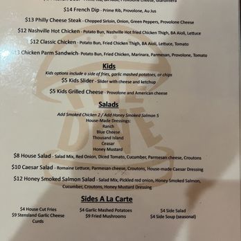 The Dive - Menu - A printed menu displays sections for Hot Sandwiches, Kids, Salads, and Sides A La Carte. Hot sandwiches include Italian Beef, French Dip, Philly Cheese Steak, Nashville Hot Chicken, Classic Chicken, and Chicken Parm Sandwich, with prices ranging from $12 to $14. Kids' options include a slider and grilled cheese, each priced at $5. Salad options include House Salad, Caesar Salad, and Honey Smoked Salmon Salad, with prices from $8 to $12. Sides include house cut fries, garlic mashed potatoes, fried mushrooms, side salad, and side soup, with prices from $4 to $9. The menu provides ingredients and optional add-ons for each dish. - Pop-Up Restaurants Near Me - Sioux Falls, South Dakota