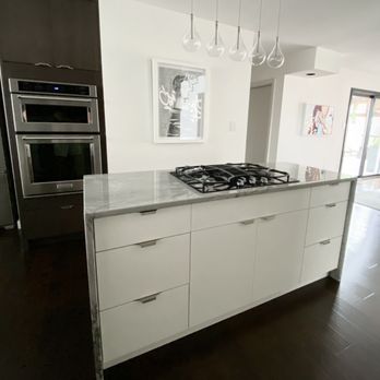 Chris Tabor Carpentry - A kitchen island with a marble surface and a built-in gas cooktop is featured in a contemporary home interior, with dark flooring and nearby appliances. - Cabinetry Near Me - Albuqueque, New Mexico