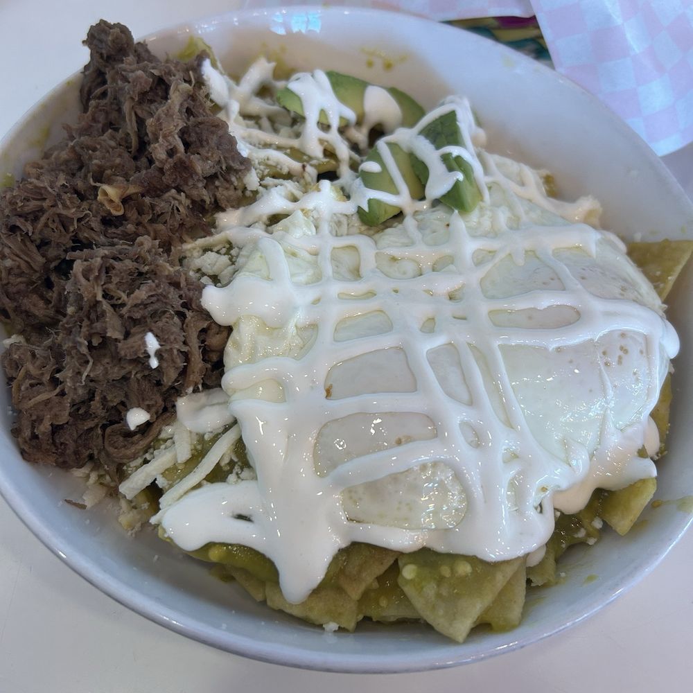 Chilaquiles topped with green salsa, two eggs over medium and a side of barbacoa