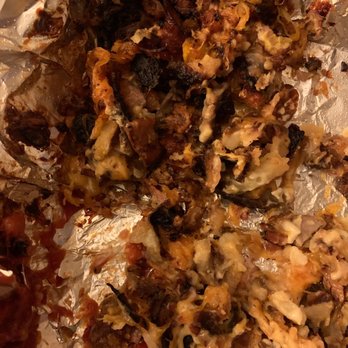 Sunnyside Grill - a pile of food wrapped in foil - The image depicts a partially consumed pizza with burnt, blackened edges and melted cheese. Toppings are visible, including meats and vegetables, on a crumpled sheet of aluminum foil. The pizza appears to have been eaten with some crust and toppings remaining, with a focus on the charred areas and melted cheese. - American Near Me - Cleves, Ohio