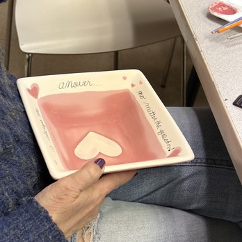 The Painted Giraffe - A ceramic plate with a pink background, a white heart, and handwritten words is held by a person. The plate has decorative hearts and text related to answering questions. - Art Classes Near Me - Westmont, Illinois