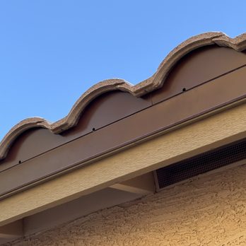 Monsoon Roofing - A detailed view of a roof with curved, clay tiles and a brown metal trim, set against a clear blue sky. - Roofing Near Me - Gilbert, Arizona