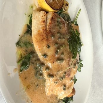 Reyes Steakhouse - Grouper in lemon caper butter sauce - amazing!! - A fish fillet is served on a white plate with green peppercorn sauce, lemon half, and greens, likely at Reyes Steakhouse in Park Ridge, IL. - Steakhouses Near Me - Park Ridge, Illinois