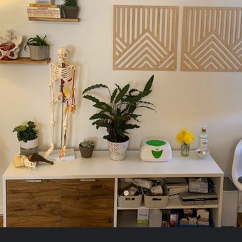 Method Physical Therapy - From their website - A white storage cabinet holds plants, a skeleton model, and decorative objects, with wall art and shelves above. - Physical Therapy Near Me - Albuquerque, New Mexico