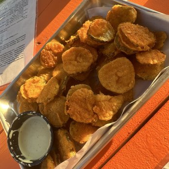 The Icehouse - Fried pickles - A metal tray contains fried pickles with a side of creamy dipping sauce, placed on an orange table outdoors. - Venues & Event Spaces Near Me - Conroe, Texas