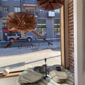 Veranda - Woven light fixtures hang above a table with stoneware plates and bowls inside a store with large window views of the street. - Home Decor Near Me - Oakland, California
