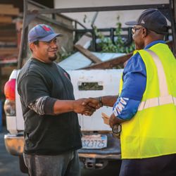 Builders FirstSource - A customer and a Builders FirstSource team member shake hands in a lumber yard next to a pickup truck carrying building mater...