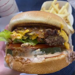 Cheeseburger with grilled onion, extra tomato, and pickles; fries (background) Cheeseburger with grilled onion, extra tomato, and pickles; fries (background)