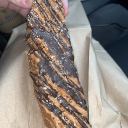 Caramel - A twisted pastry with a crispy exterior is decorated with chocolate and caramel drizzle and sprinkled with coarse salt, served on brown parchment paper.