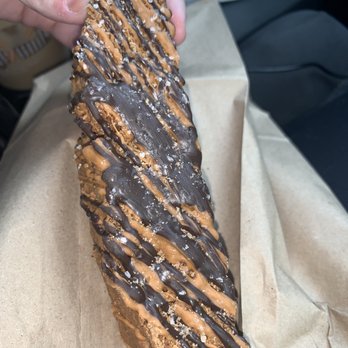 Common Grounds - Salted Caramel Biscotti - A twisted pastry with a crispy exterior is decorated with chocolate and caramel drizzle and sprinkled with coarse salt, served on brown parchment paper. - Coffee Roasteries Near Me - Shelton, Connecticut