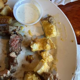 steak bites and garlic bread. - A plate with steak bites, pieces of garlic bread, and a small cup of ranch dressing, served at a restaurant.