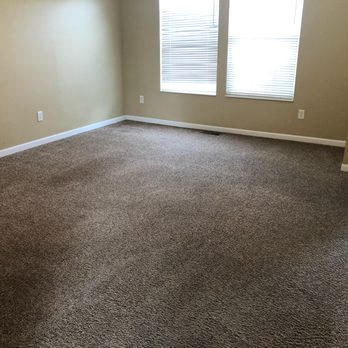 Walker Cleaning Services - Close up of the front room. - A vacant room featuring beige walls, a brown carpeted floor, and two windows with closed blinds, with electrical outlets visible. - Carpet Cleaning Near Me - Cincinnati, Ohio