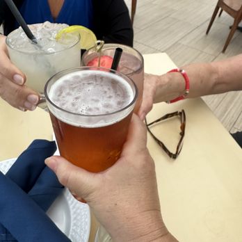 Offshore Rooftop - Yummy drinks - Three individuals are raising their glasses in a toast, with drinks including beer and cocktails, at a dining establishment. - New American Near Me - Chicago, Illinois