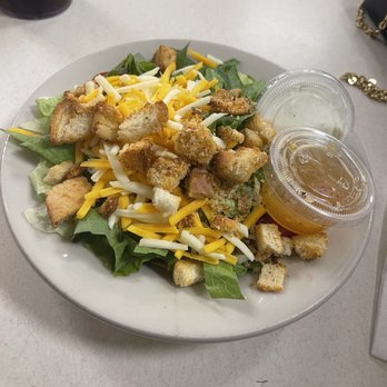 Red Squirrel - Side salad! - A plate contains a side salad with green lettuce, shredded cheddar and mozzarella cheese, and toasted croutons. Two small clear containers hold salad dressing, one with a creamy white dressing and the other with a vinaigrette. The plate is placed on a light-colored table, with a dark drink and a black purse visible in the background. - Diners Near Me - Cincinnati, Ohio
