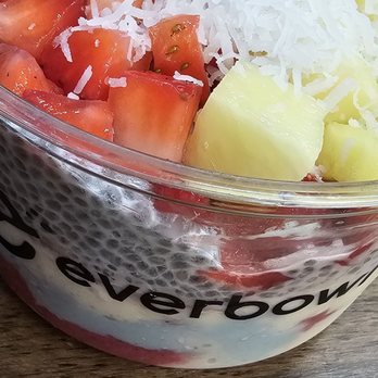 Everbowl - Blue lagoon - A fruit salad in a clear glass bowl contains strawberries, pineapple chunks, shredded cheese, and shredded coconut, placed on a wooden surface. - Acai Bowls Near Me - Gilbert, Arizona