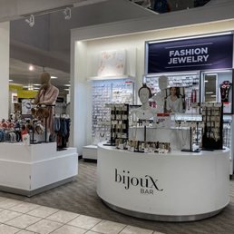A jewelry and fashion accessories kiosk is situated inside a retail store, featuring necklaces, earrings, and bracelets on display.