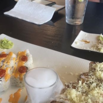 Swordfish - In restaurant Godzilla roll and spicy salmon meal - Sushi dishes are on a table with a glass of water with lemon and a drink emitting dry ice smoke, in a restaurant setting. - Sushi Bars Near Me - Batavia, Illinois
