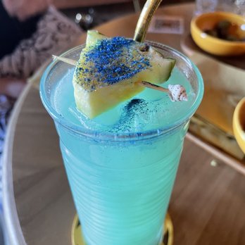 Honey Elixir Bar - A tropical drink with blue curaçao! - A vibrant blue tropical cocktail with a pineapple slice and blue sugar on top, served in a tall glass with a straw. - Lounges Near Me - Denver, Colorado