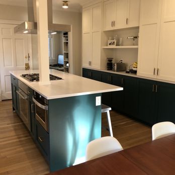 Northwoods Builders - Kitchen - The kitchen has white upper cabinets, dark lower cabinets, and a white countertop island with a built-in stove. There are small ceiling lights and kitchen appliances on the counter. - General Contractors Near Me - Acton, Massachusetts
