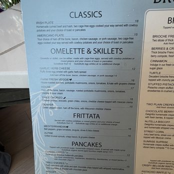 Brunch Berry - A menu board from a brunch restaurant features sections for classics, omelettes, and pancakes. Items include Irish Plate, Americano Plate, garlic herb cheese omelette, farm fresh veggie omelette, and various pancake options. The menu provides detailed descriptions and prices for each dish, with some options offering substitutions or additional charges. The board is set against a background with some plants and other objects visible at the top. - Coffee & Tea Near Me - New Berlin, Wisconsin